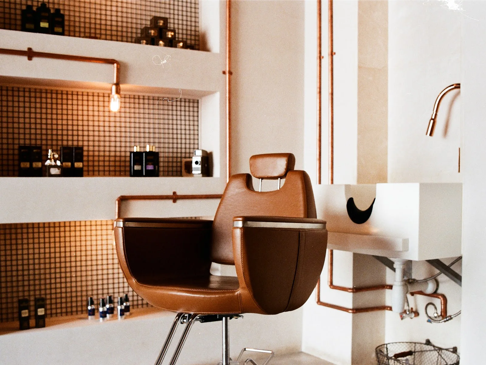 Tan leather barber chair beside white walls with exposed copper pipes