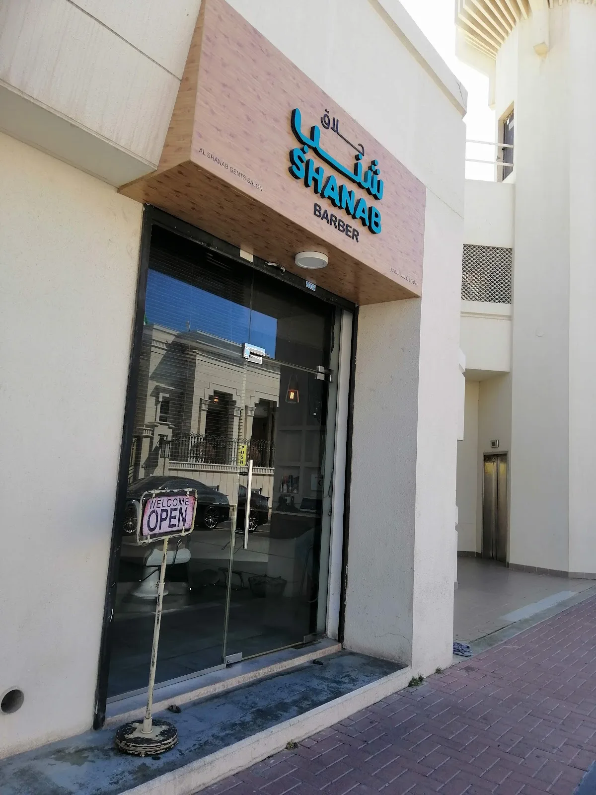 Glass entrance door of Shanab Barber with a welcome open sign