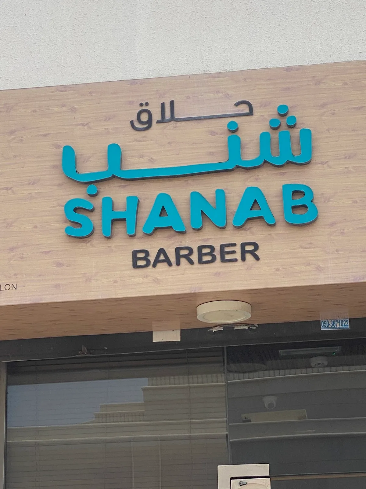 Close-up of the teal Shanab Barber sign on a wood panel