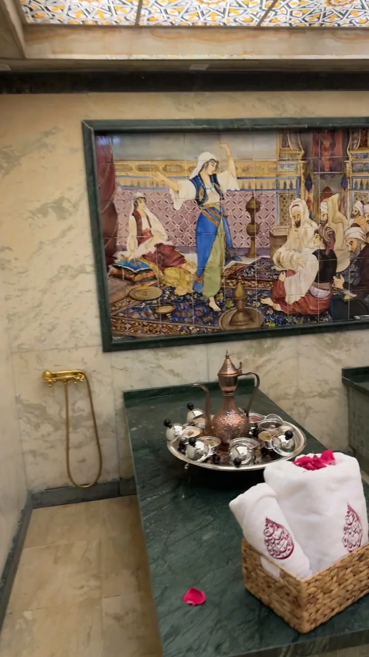 Marble hammam with tiled mural, copper teapot and rolled towels
