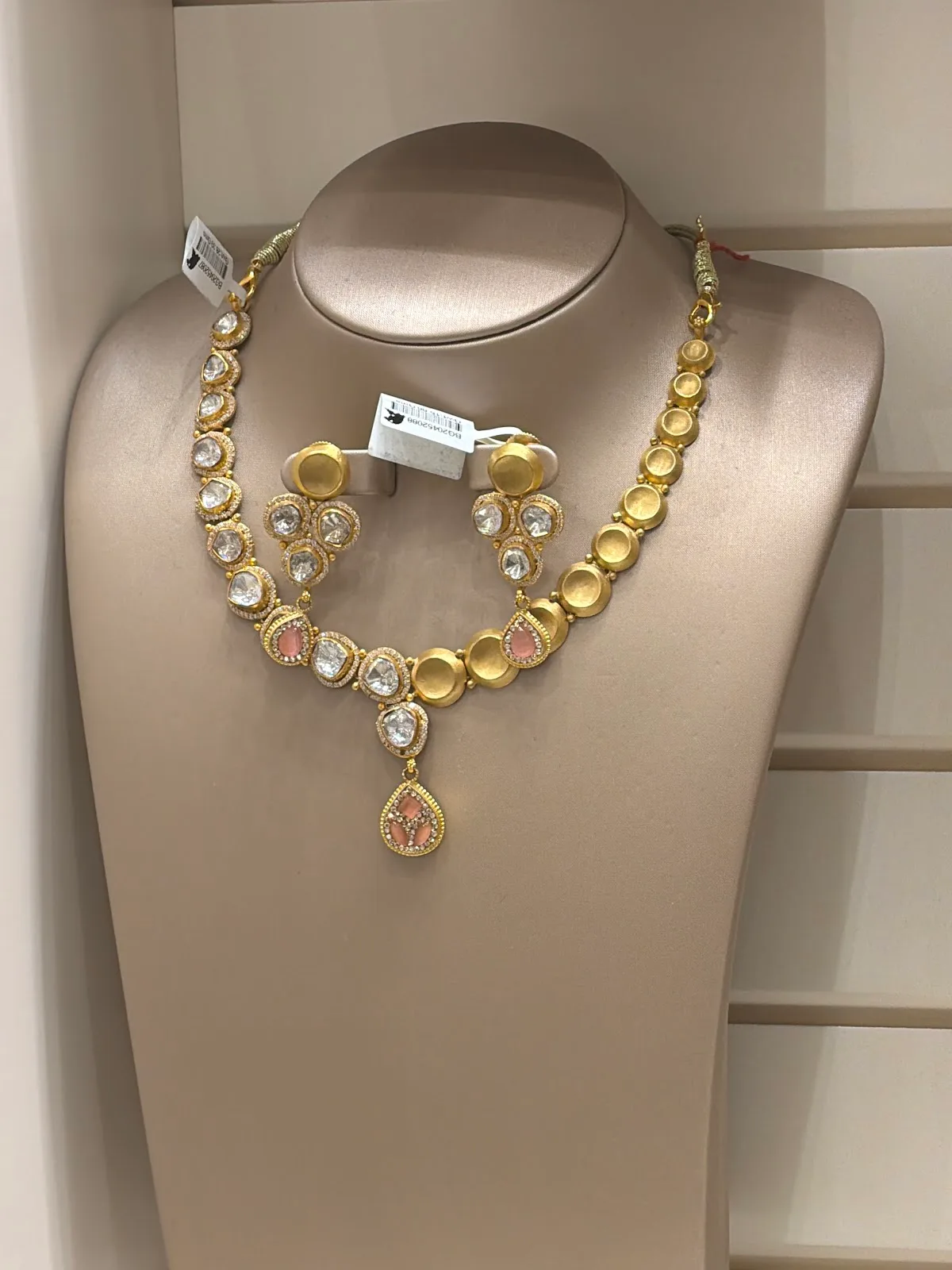 Gold necklace and earring set with coral and clear stones on a display bust at Mega Star Jewellers