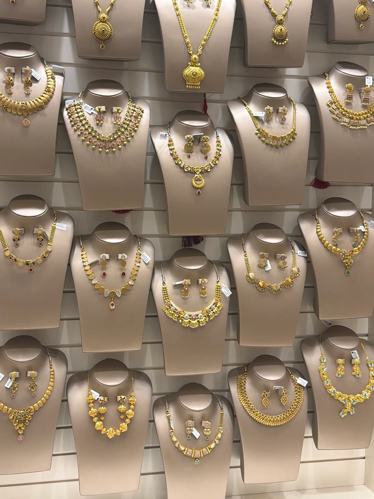 Wall of gold necklace and earring sets on display busts