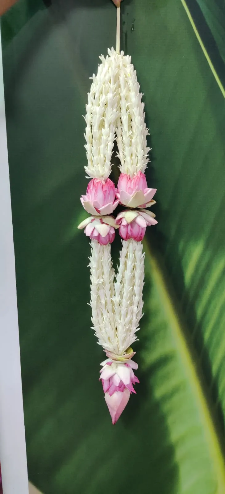 A jasmine and pink lotus temple garland hanging against a green banana leaf, handmade at Jasmine Experts