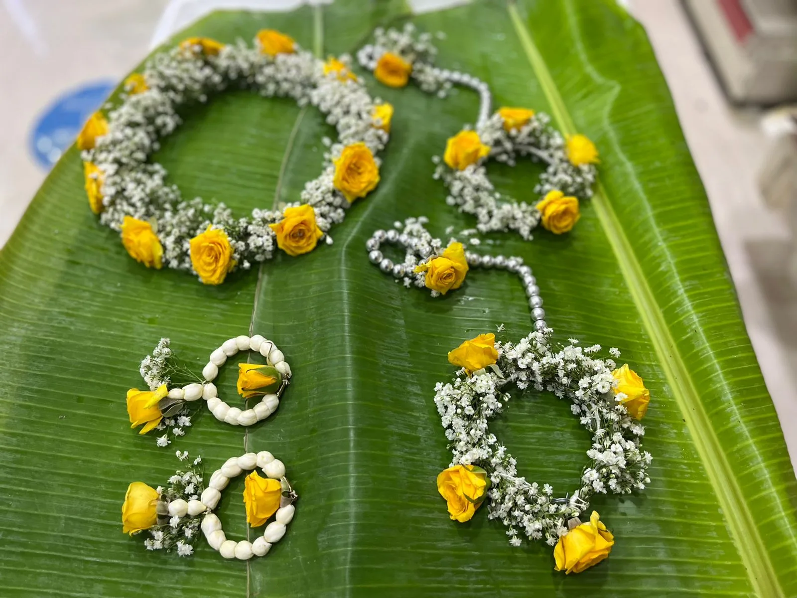 Yellow rose and baby's breath floral jewellery set laid on a banana leaf