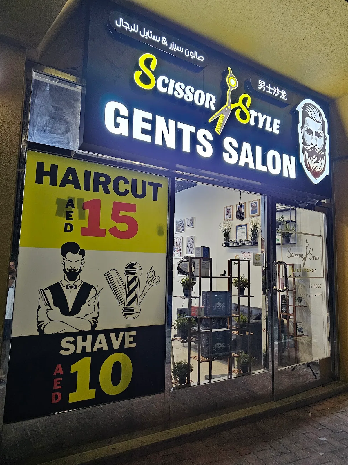 Scissor & Style Gents Salon illuminated shopfront at night showing haircut AED 15 and shave AED 10 signage