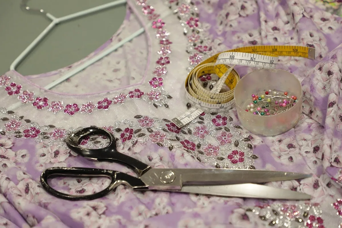 Tailor's shears and a measuring tape resting on a floral fabric being embellished with beadwork