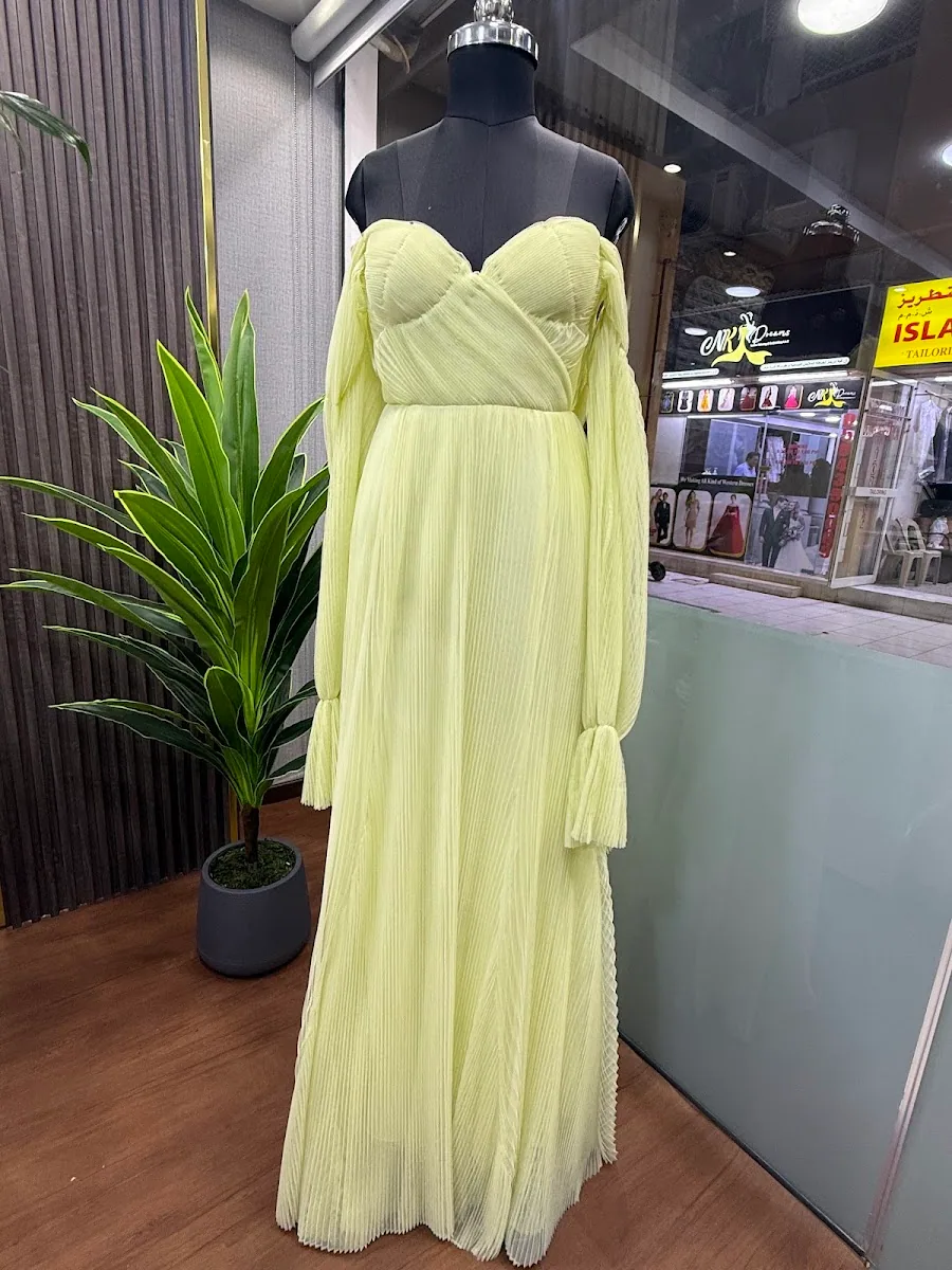 Pale yellow pleated chiffon gown with draped sleeves displayed on a mannequin inside the atelier