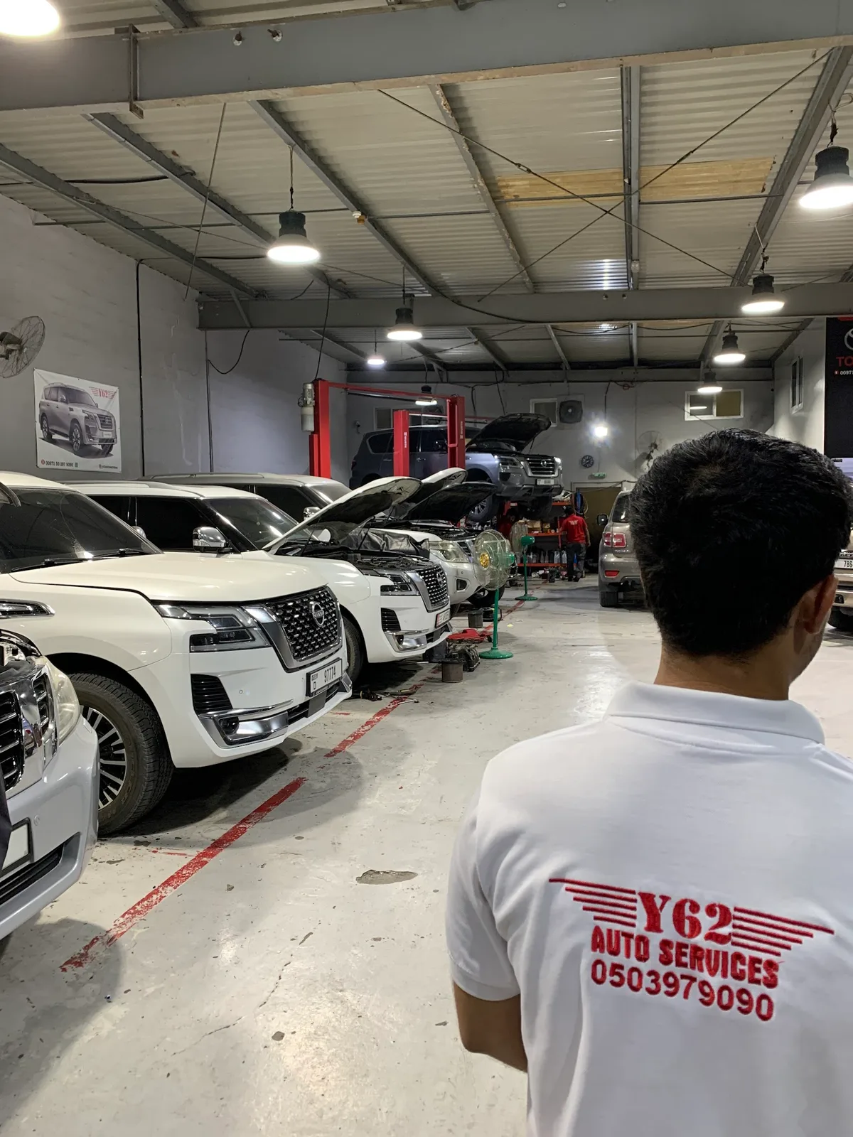 Y62 Auto Services technician in a branded shirt beside Nissan Patrols being serviced in the workshop