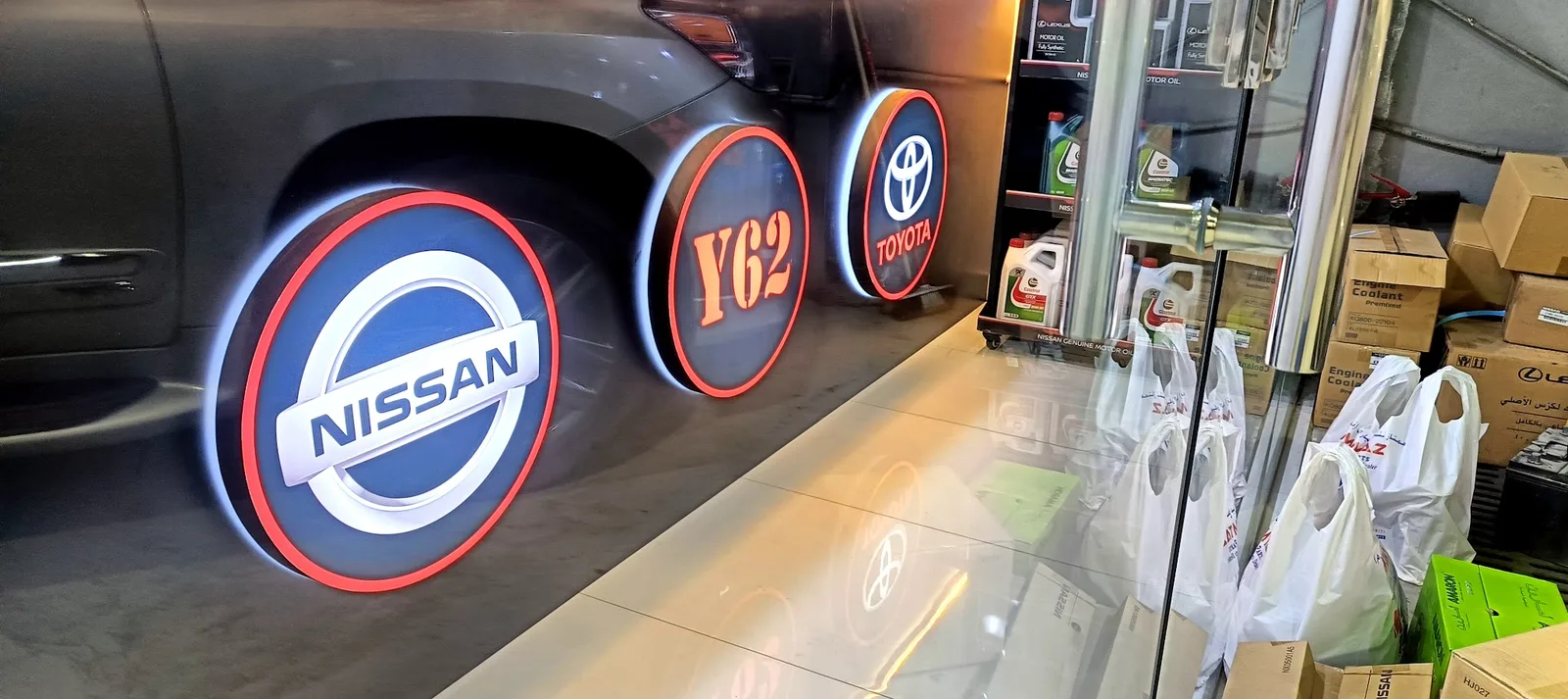 Backlit Nissan, Y62 and Toyota badges mounted on the workshop wall above branded motor oil