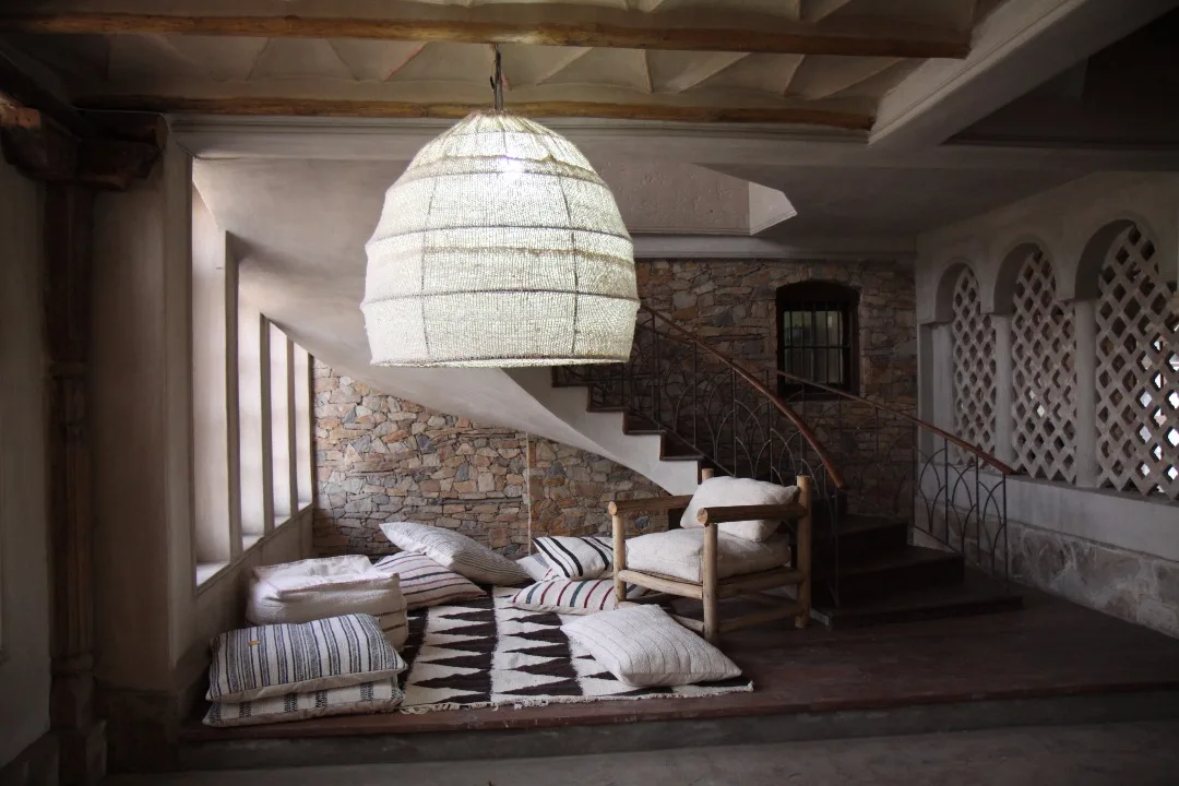 A floor-cushion corner beneath a woven pendant in a rustic stone interior