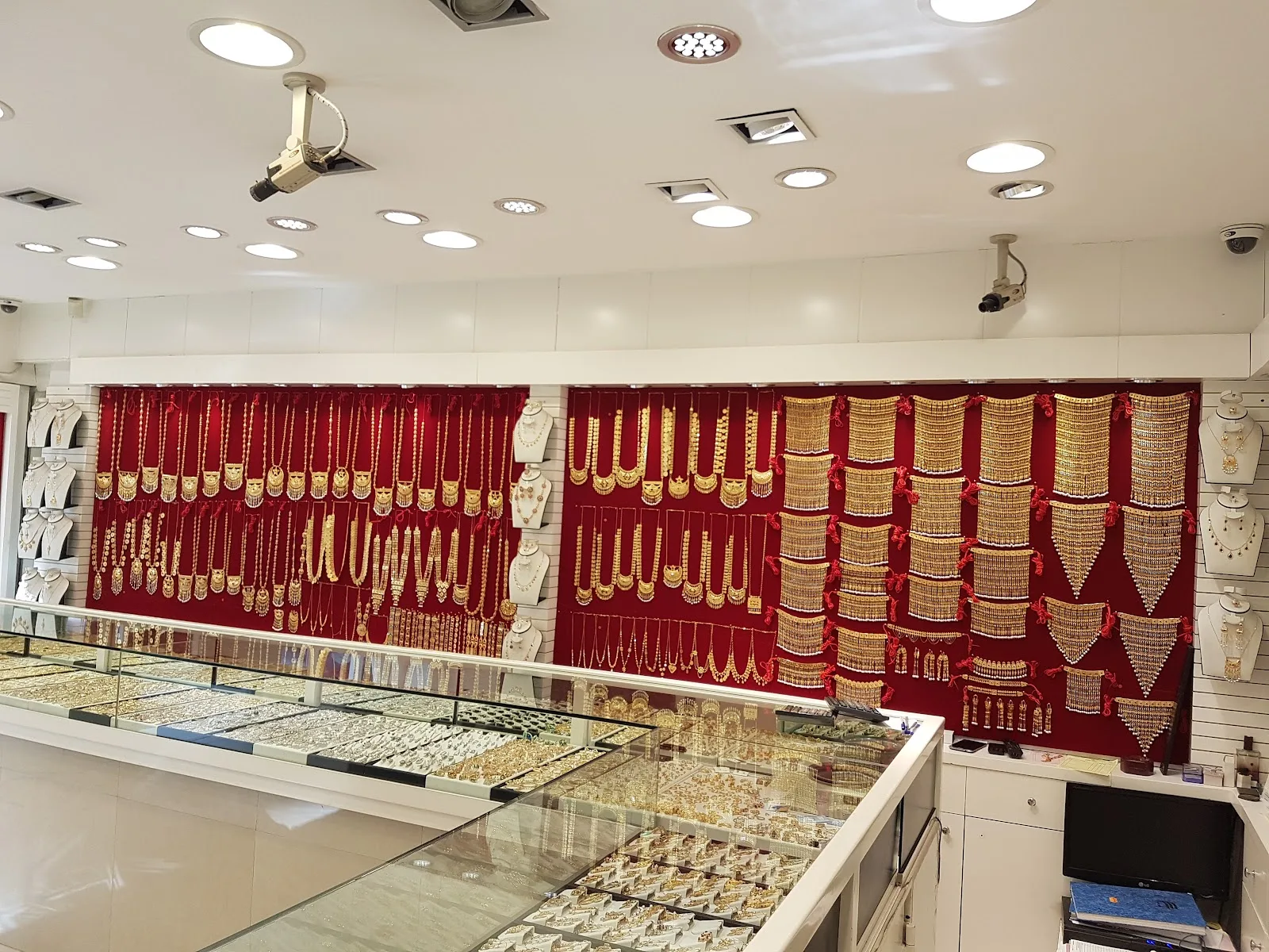 Wide red velvet wall hung with gold necklaces above lit glass counters